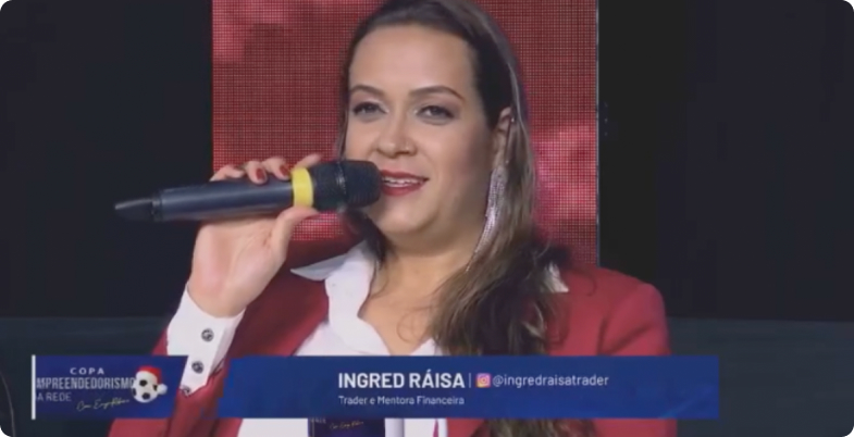 Ingred Ráisa parle dans un micro, vêtue d'une veste rouge sur une chemise blanche.