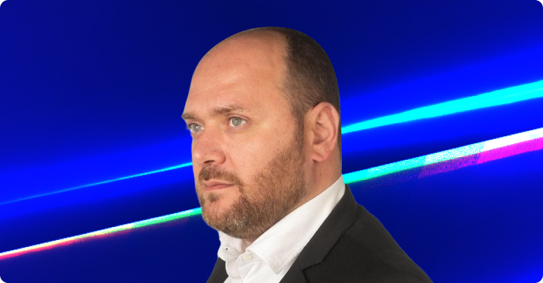 Um homem em terno e camisa branca contra um fundo azul com faixas de luz coloridas.