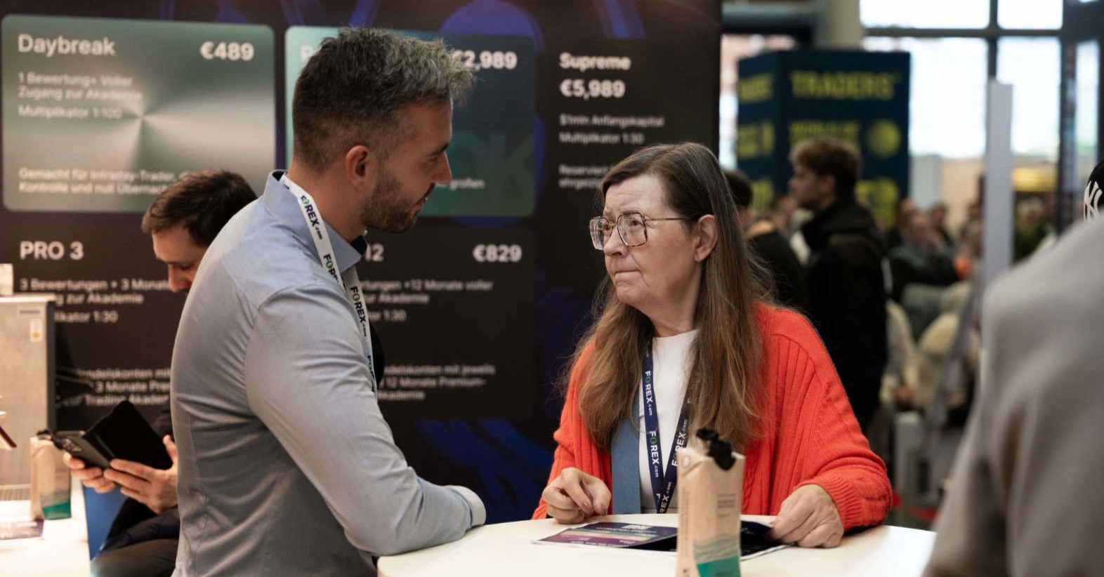 Un homme et une femme discutent à un stand avec des bannières promotionnelles en arrière-plan.